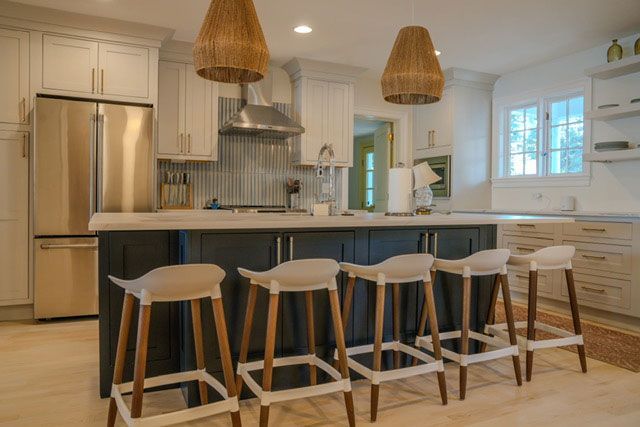 Modern kitchen with white cabinets, stainless fridge, blue island, and four bar stools under woven pendant lights