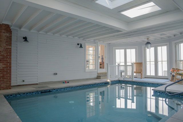 Indoor swimming pool with white paneled walls, skylights, and chairs by the windows