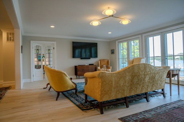 Modern living room with yellow sofas, wall-mounted TV, and large windows overlooking water