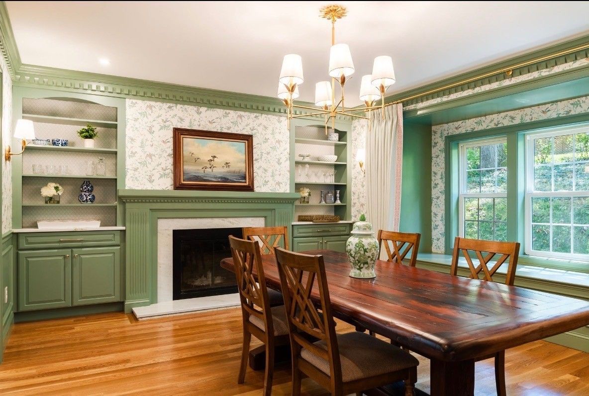 Elegant dining room with green walls, fireplace, chandelier, and a wooden table with chairs