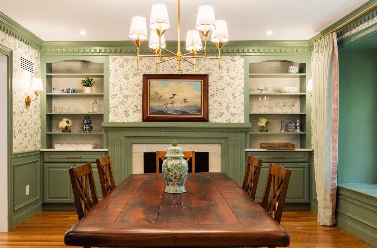 Elegant dining room with green built-ins, a wooden table, chandelier, and fireplace