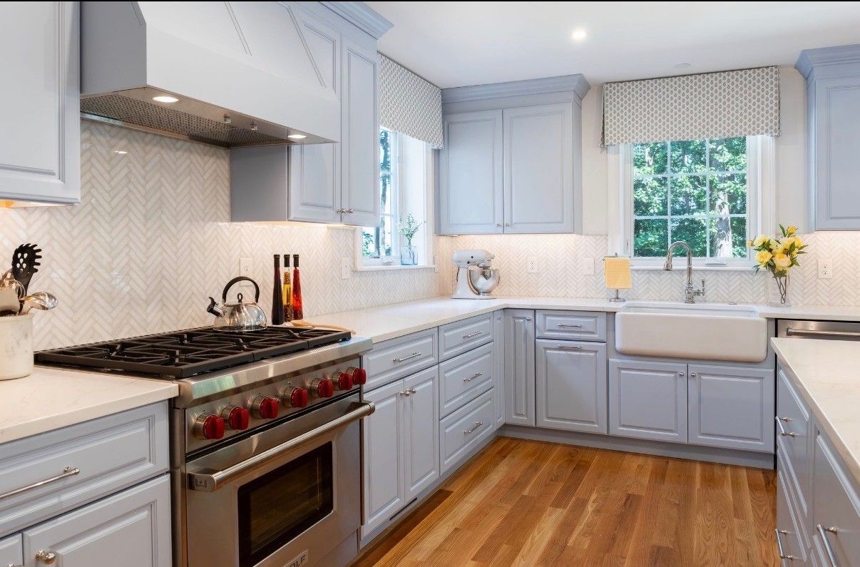 Bright modern kitchen with gray cabinets, stainless steel appliances, white tile backsplash, and wood floors