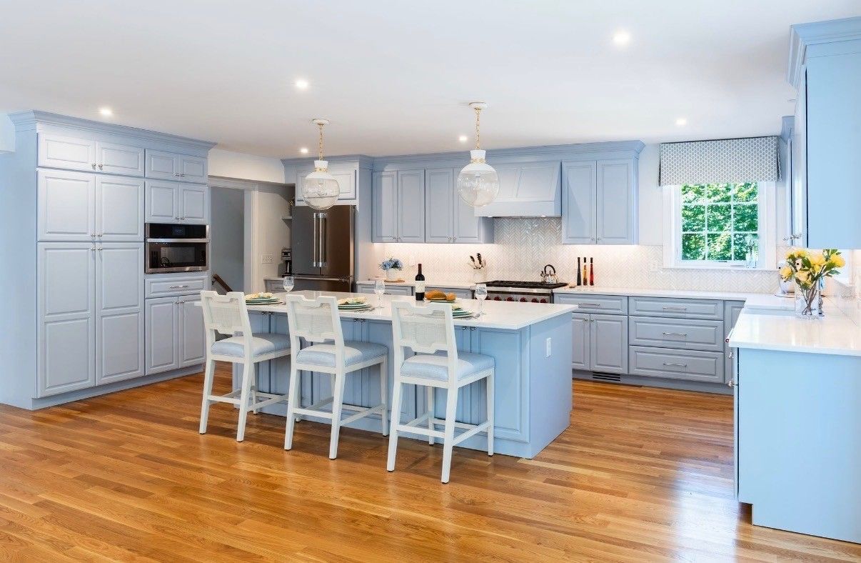 Bright blue modern kitchen with island, white bar stools, stainless appliances, and hardwood floors