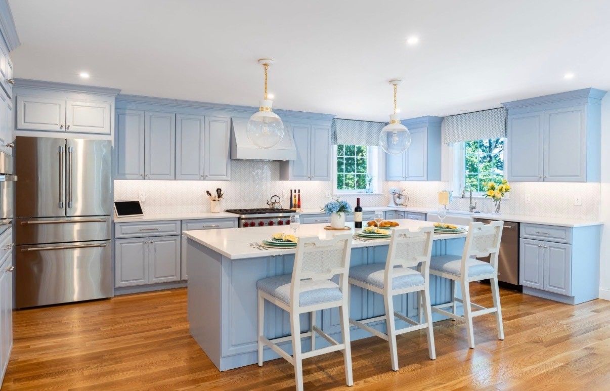Bright modern kitchen with light blue cabinets, stainless steel fridge, island, and white barstools