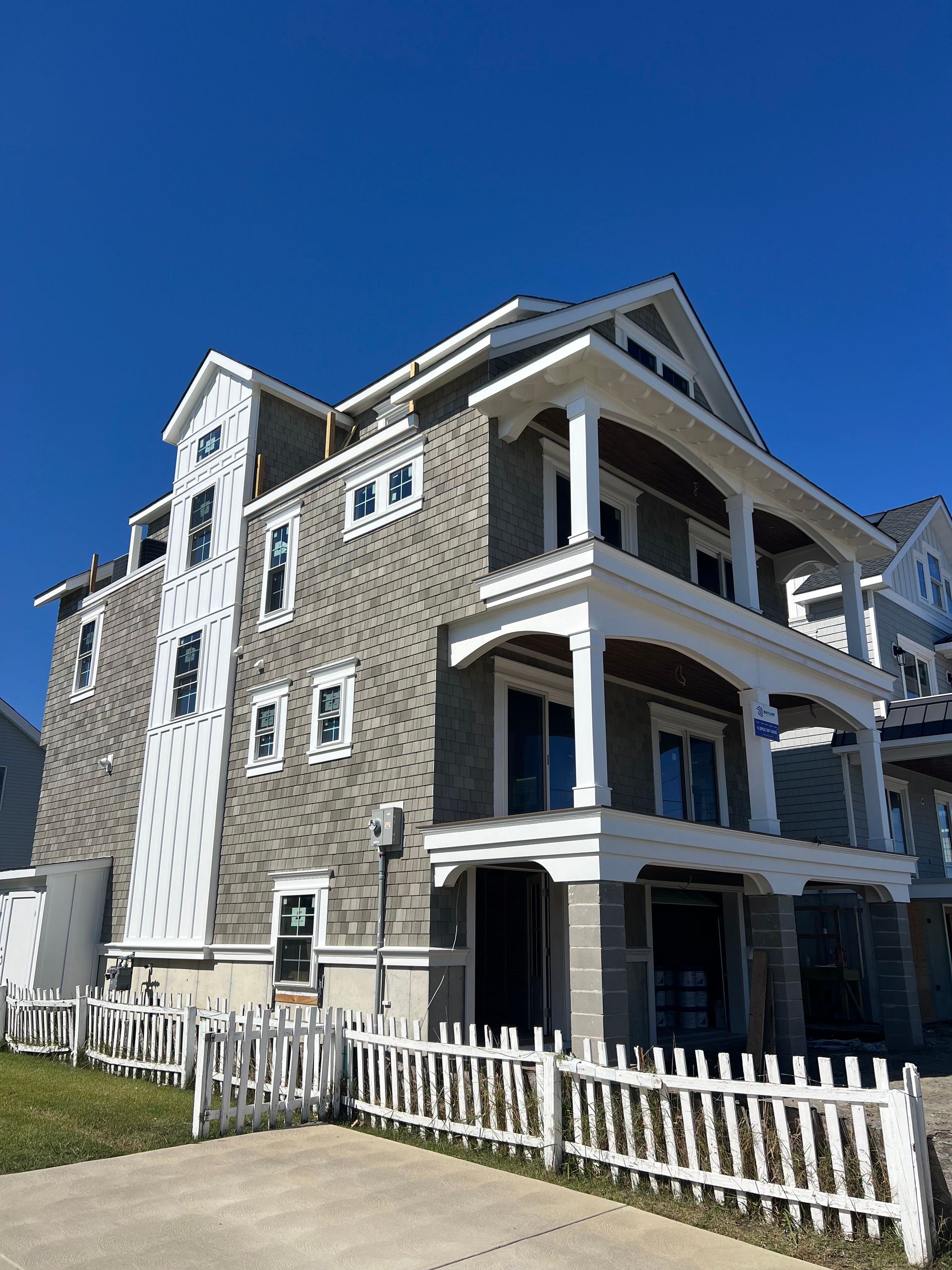 Three-story gray house with white trim and porch behind a white picket fence under a blue sky