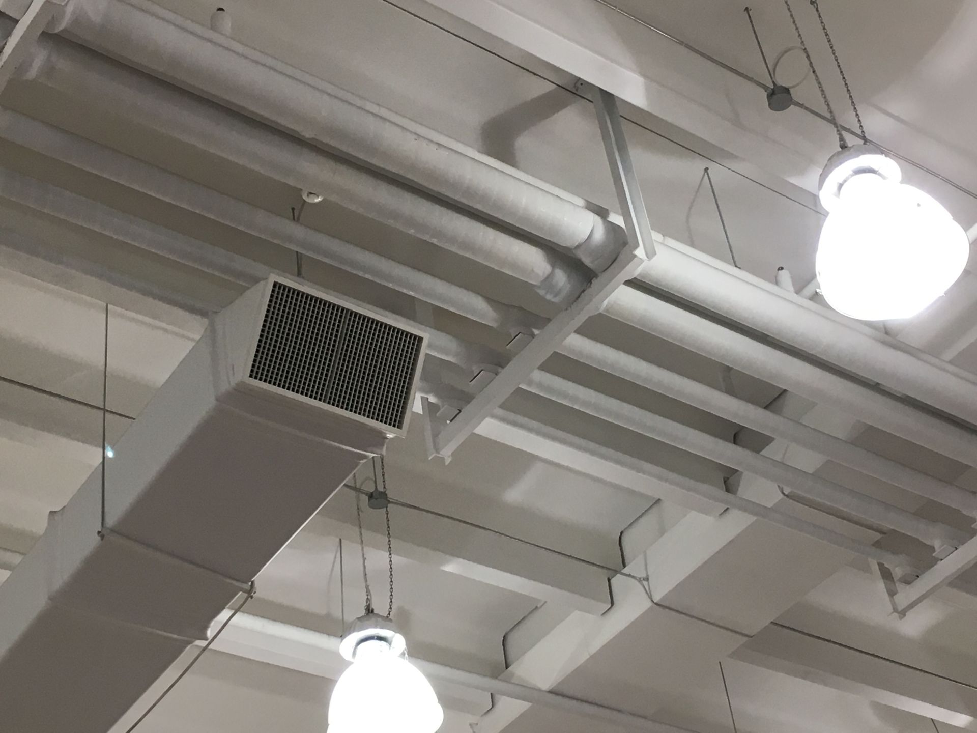 White ceiling with ducts, pipes, lights, and support beams.