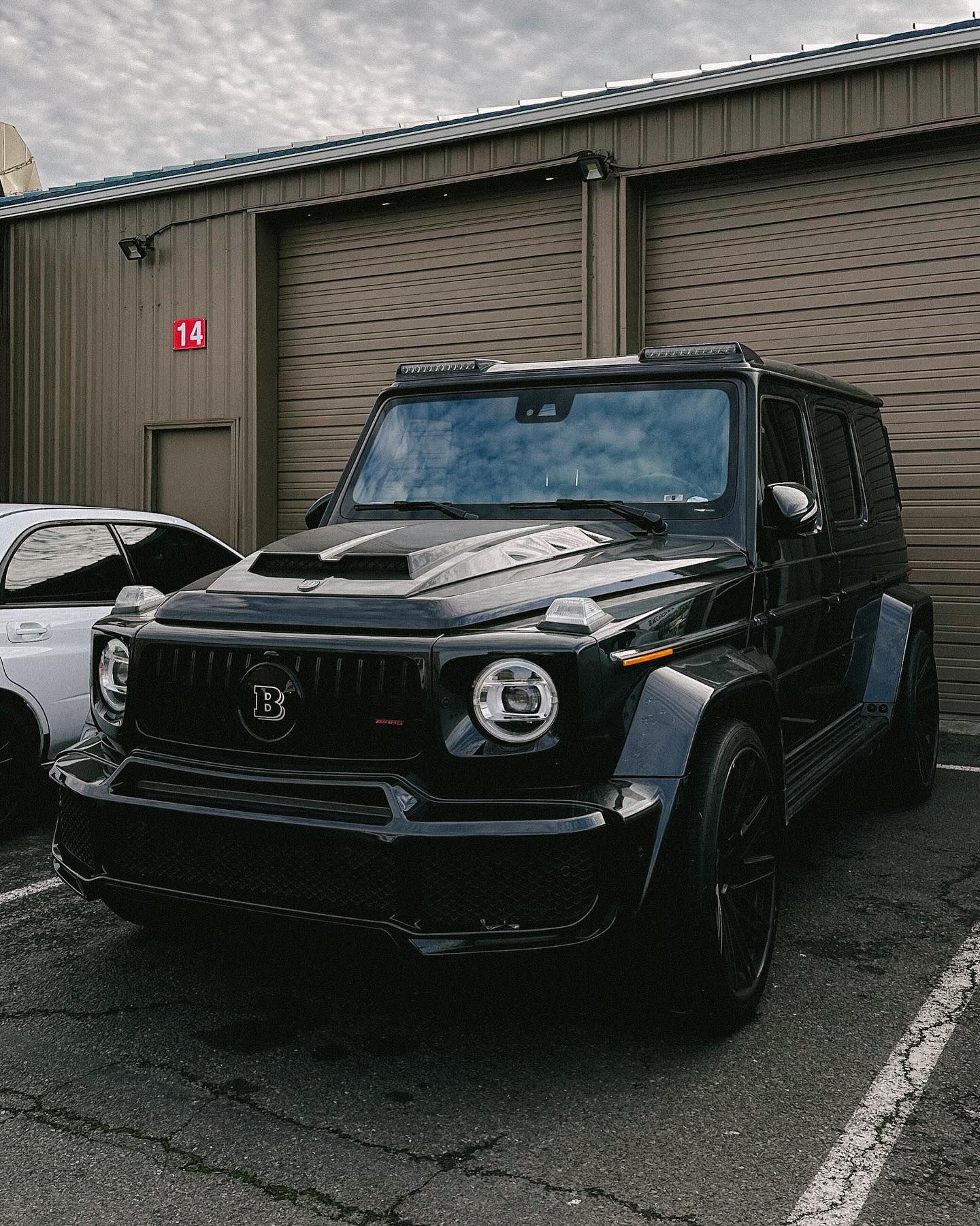 Black Mercedes-Benz G-Wagon parked in front of a corrugated metal building on an overcast day.