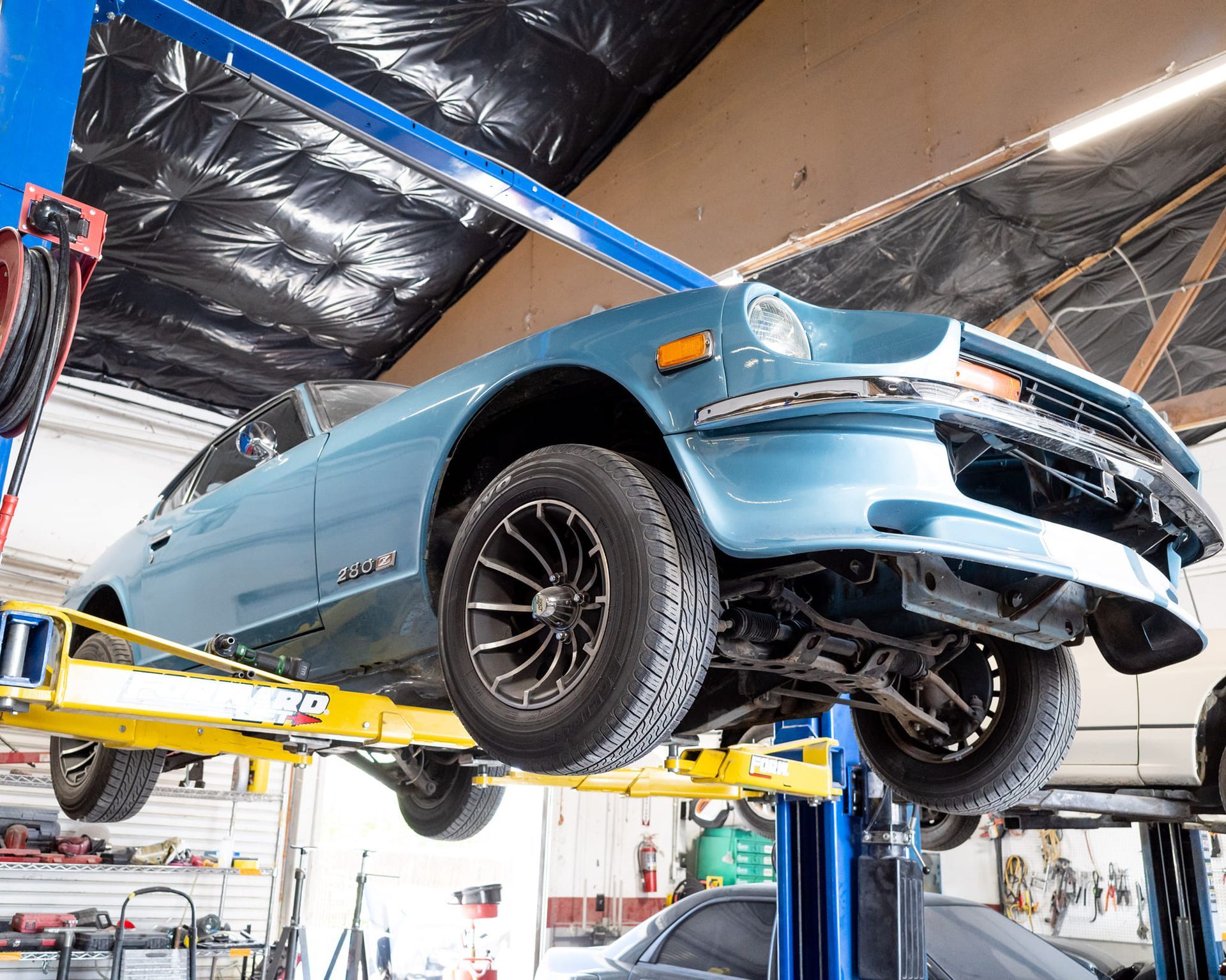Blue vintage car lifted on a yellow car lift inside a garage.