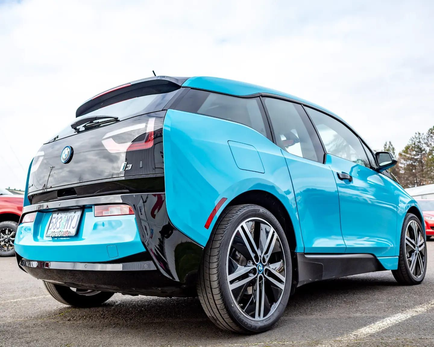 Blue BMW i3 electric car, rear view, on pavement with black accents.