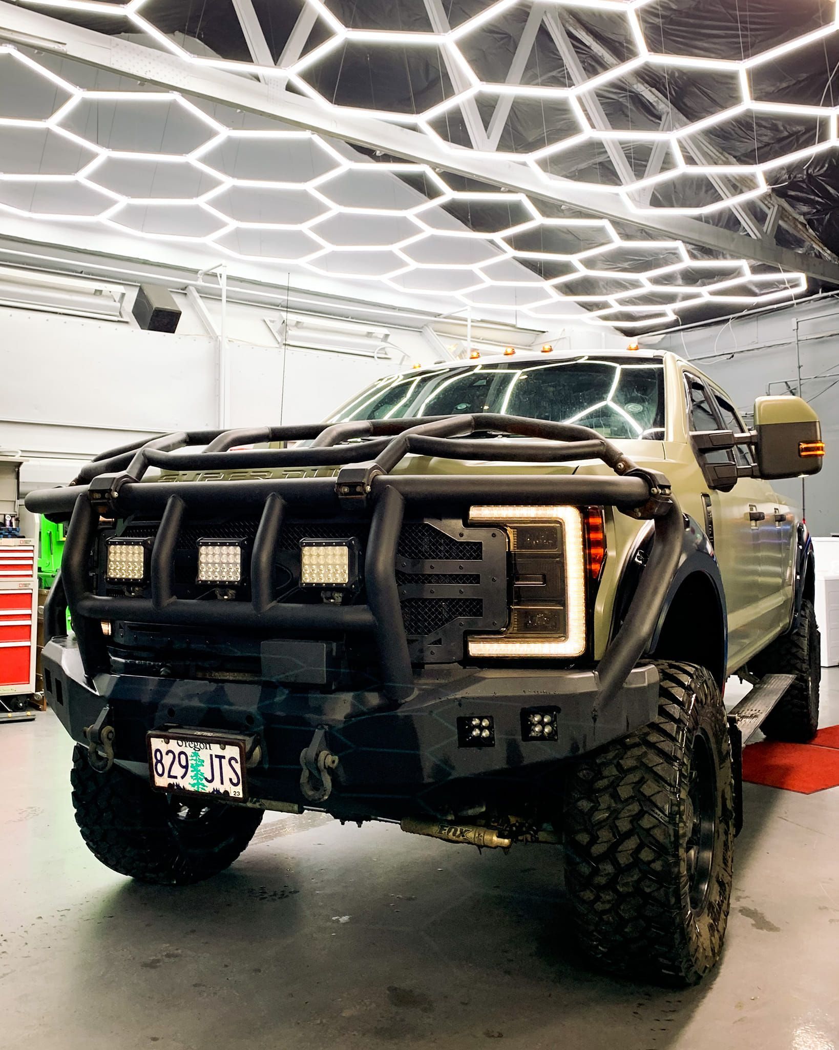 Olive green lifted truck with black brush guard, under hexagon lights.