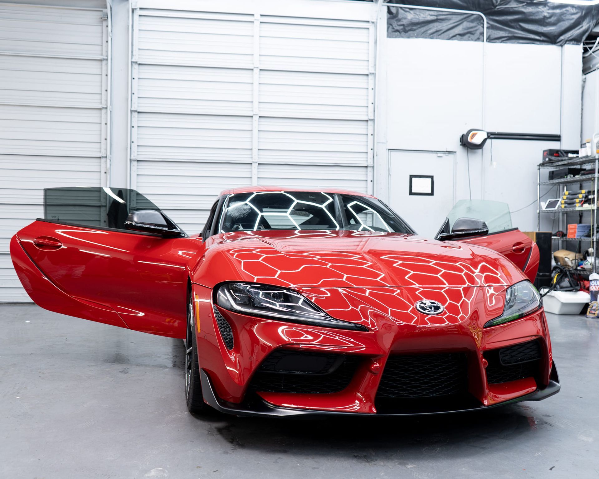 Red Toyota Supra sports car with open doors in a garage.