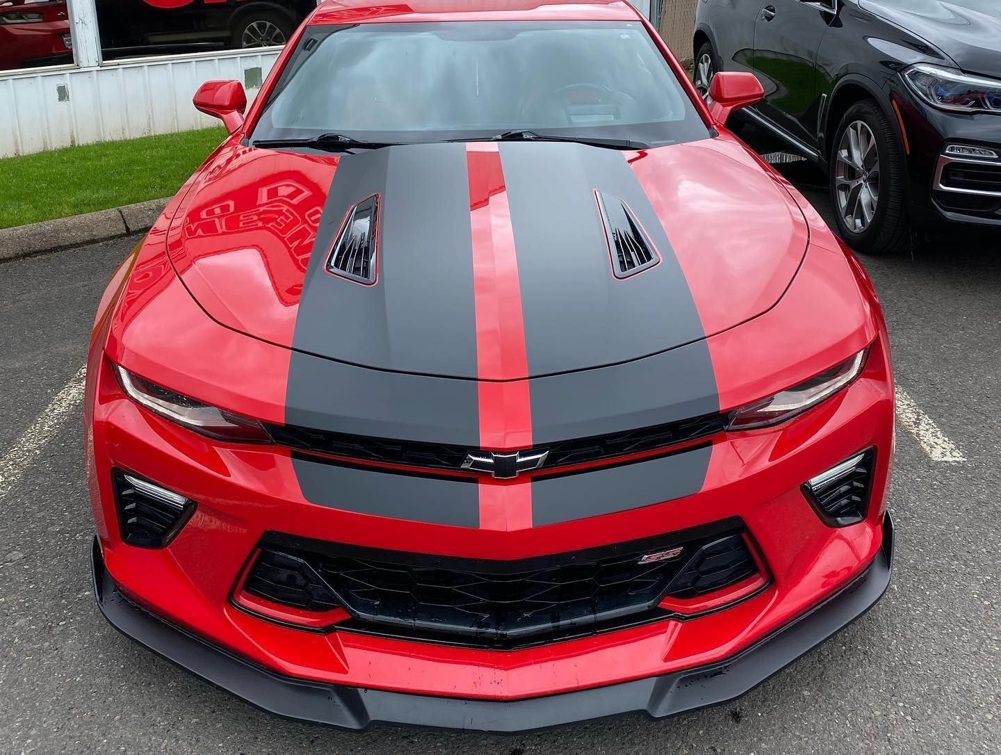 Red Chevrolet Camaro with black racing stripes on the hood, parked outside.