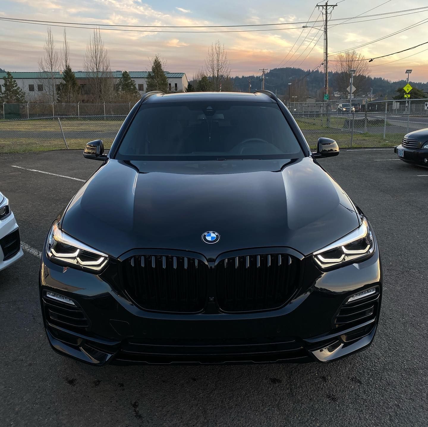 Black BMW SUV parked outdoors, front view. Black grill, headlights on, overcast sky.