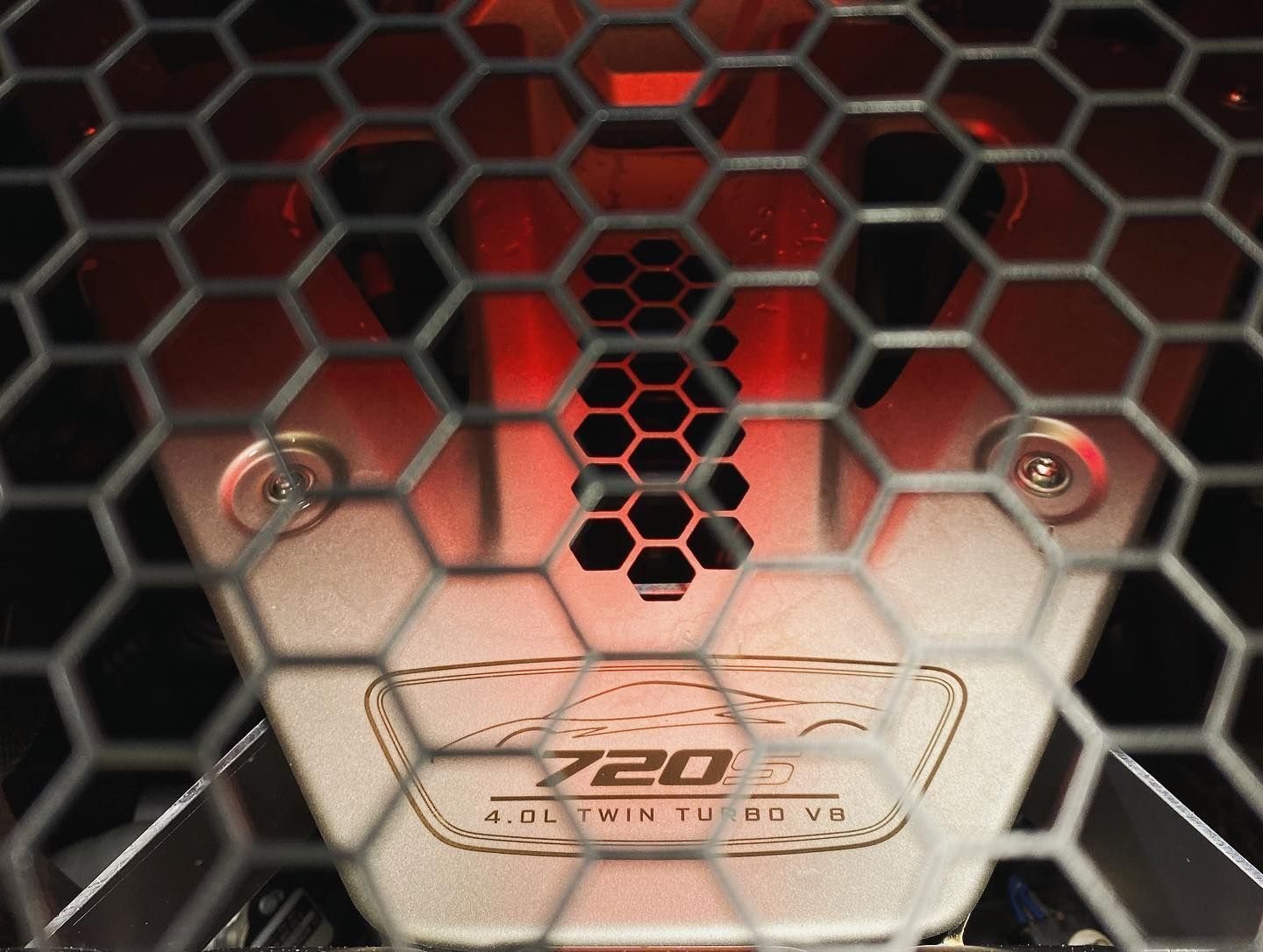 Close-up of a McLaren 720S engine bay. Honeycomb grill with red lighting.