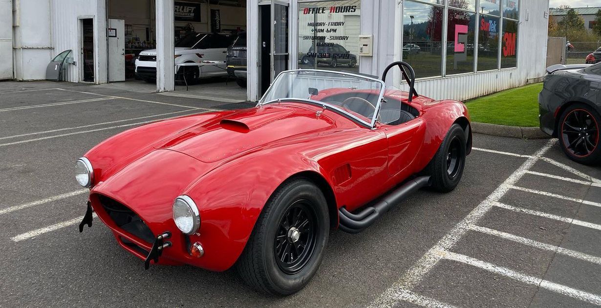 Red classic roadster parked in front of a building with black wheels and a roll bar.