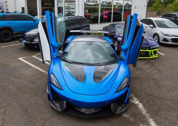 Blue sports car with gull-wing doors open, parked in front of a building.