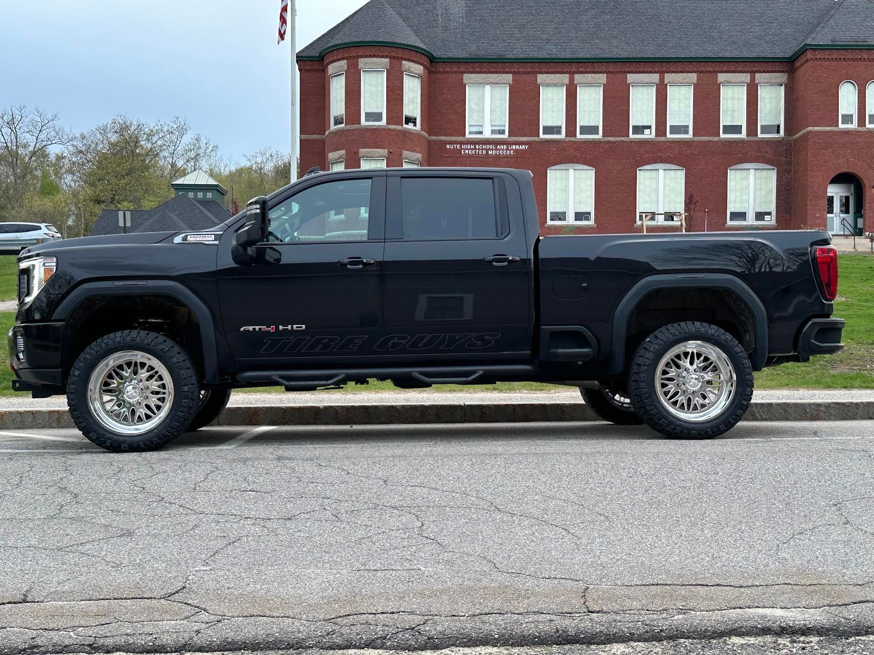 A black truck is parked on the side of the road in front of a brick building.