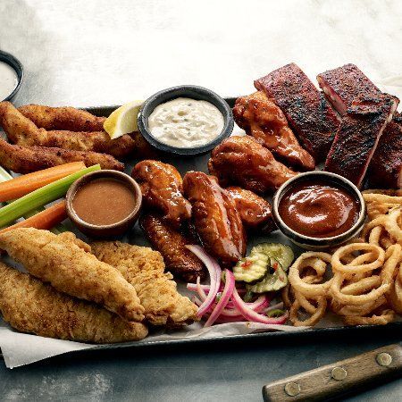 Appetizer platter with fried chicken, ribs, wings, onion rings, sauces, and vegetables.