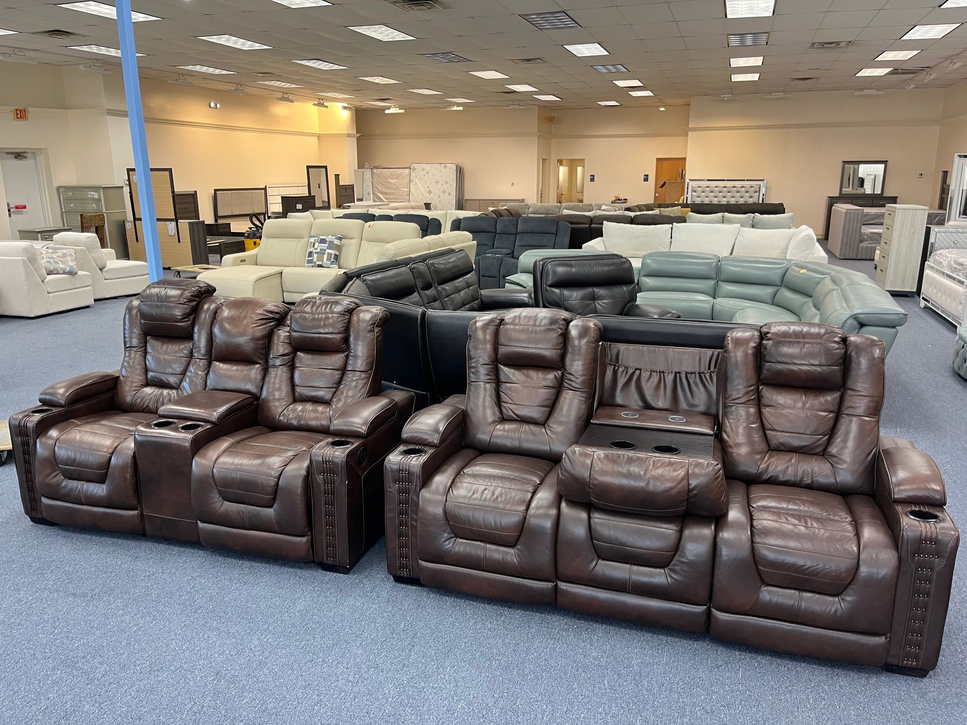 Furniture showroom with brown and gray leather recliner sofas on a blue carpeted floor.