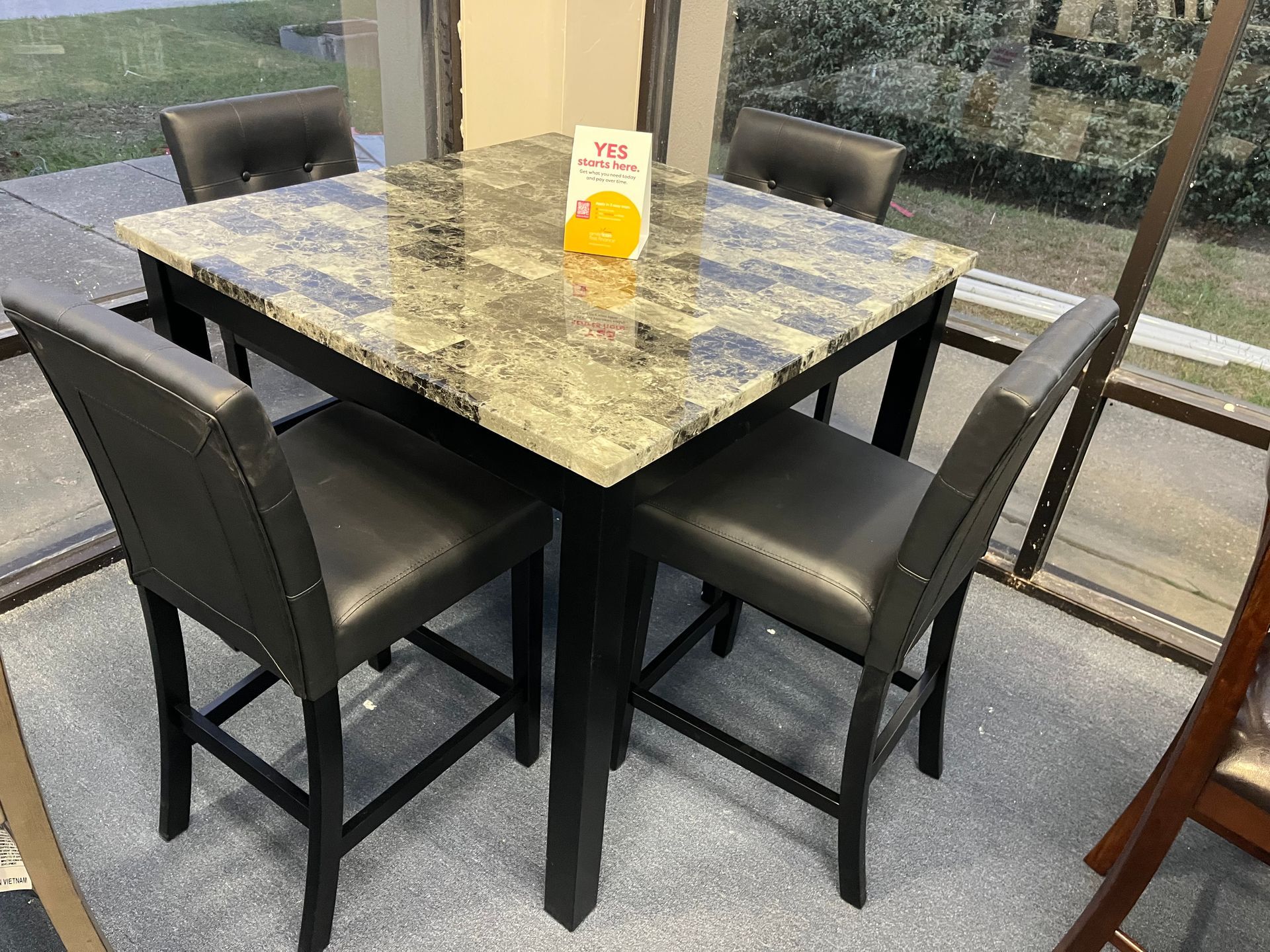 Small café table with four black chairs and a menu sign in a bright windowed seating area