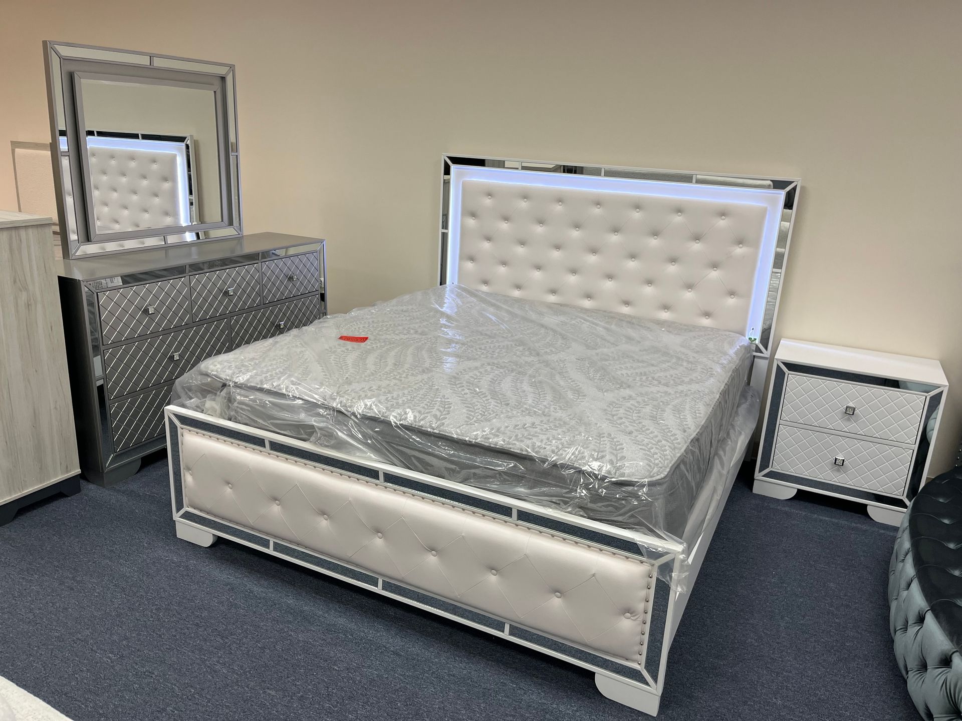 Modern tufted bed with mirrored dresser and nightstand in a showroom or bedroom display