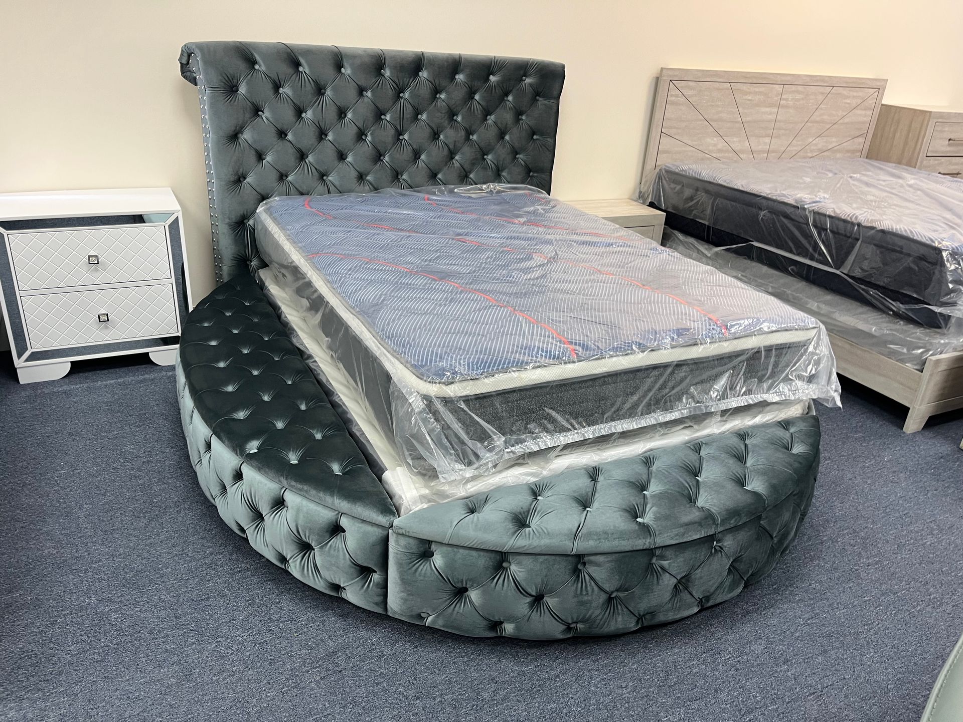 Upholstered round bed frame with tall tufted headboard in a furniture showroom, with mattresses on top.