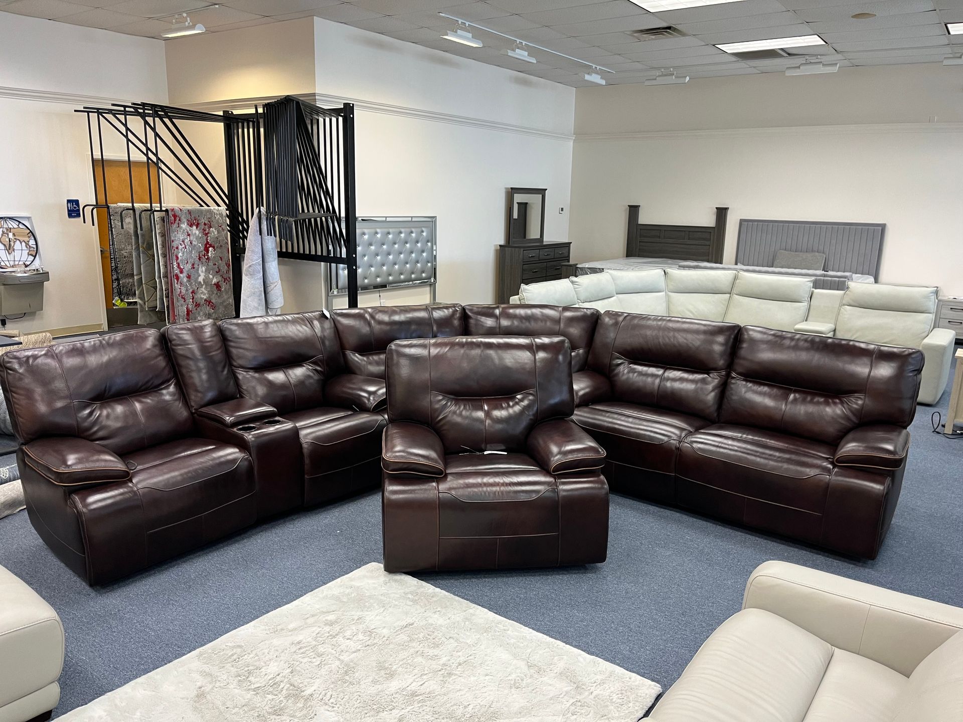 Brown leather sectional sofa set in a showroom with light-colored chairs and blue carpet
