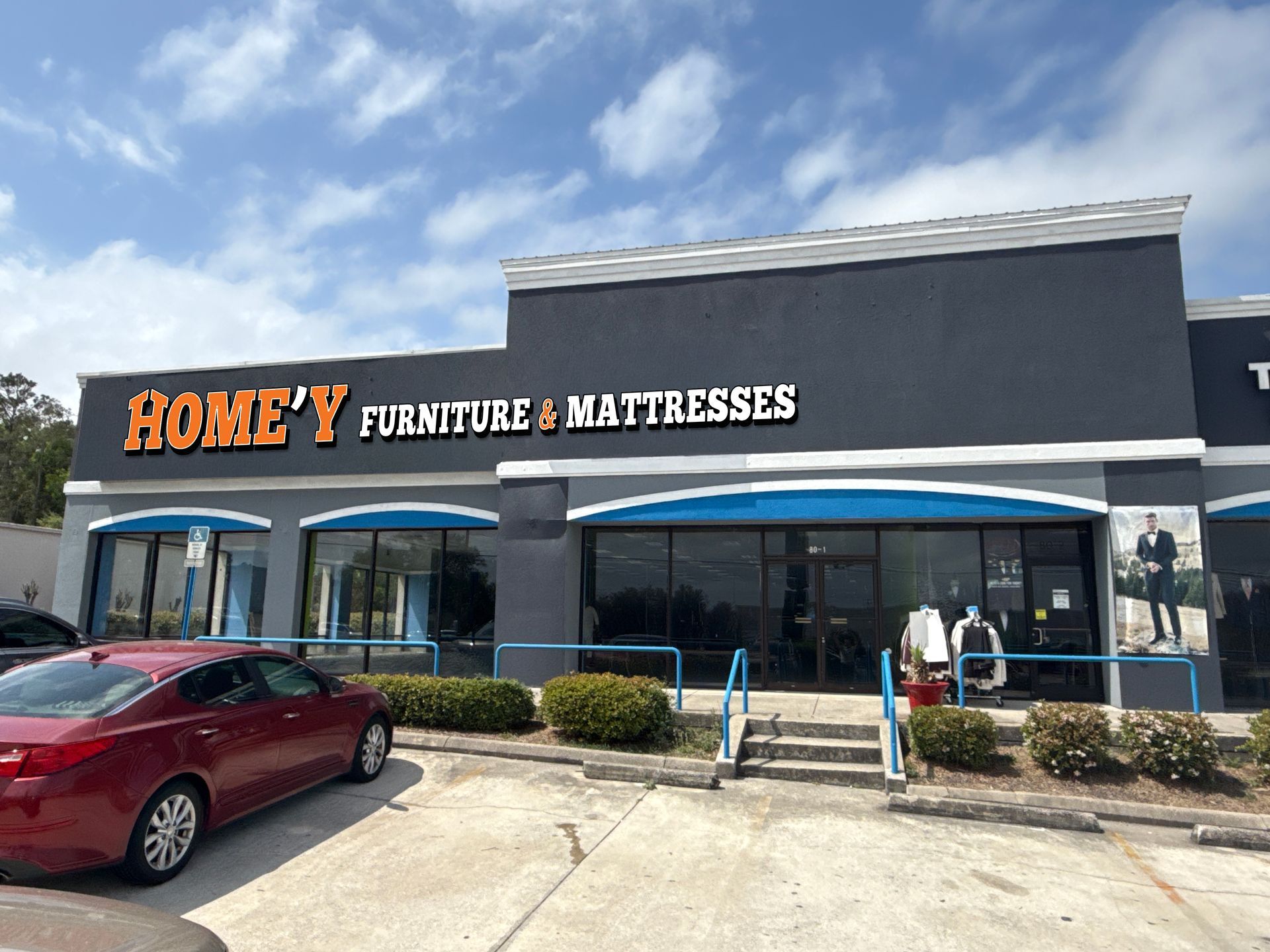 Furniture and mattress store storefront with blue awnings and a red car parked outside