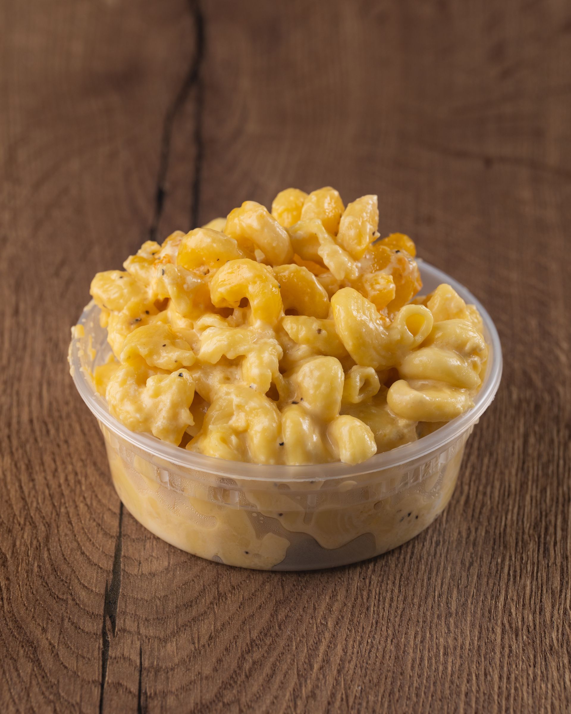 Mac and cheese in a clear plastic container on a wooden surface.