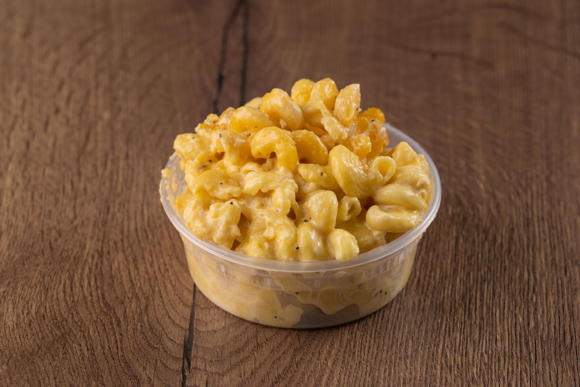 Mac and cheese in a clear plastic container on a wooden surface.