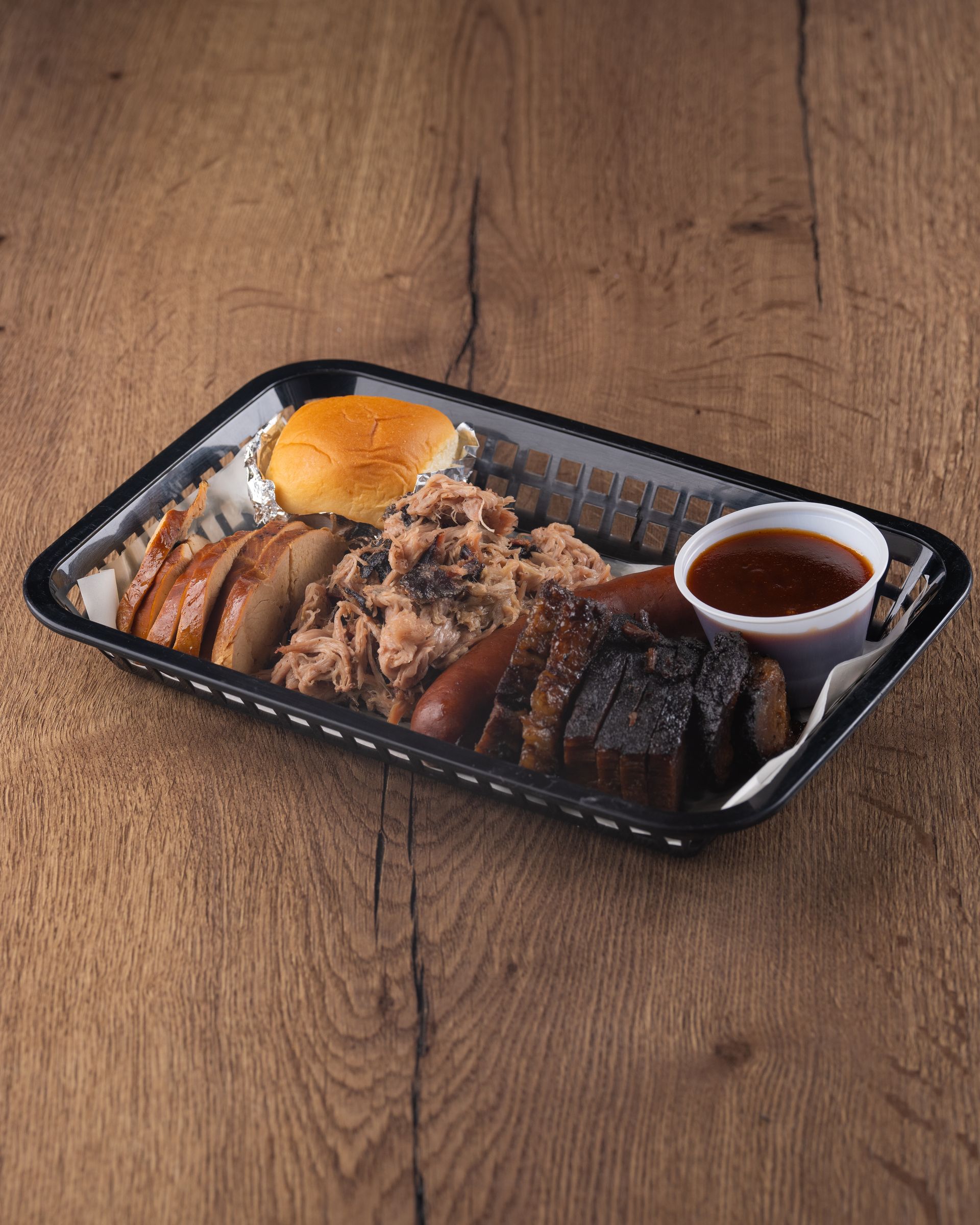 BBQ platter with sliced brisket, sausage, pulled pork, and sauce, on a wooden table.