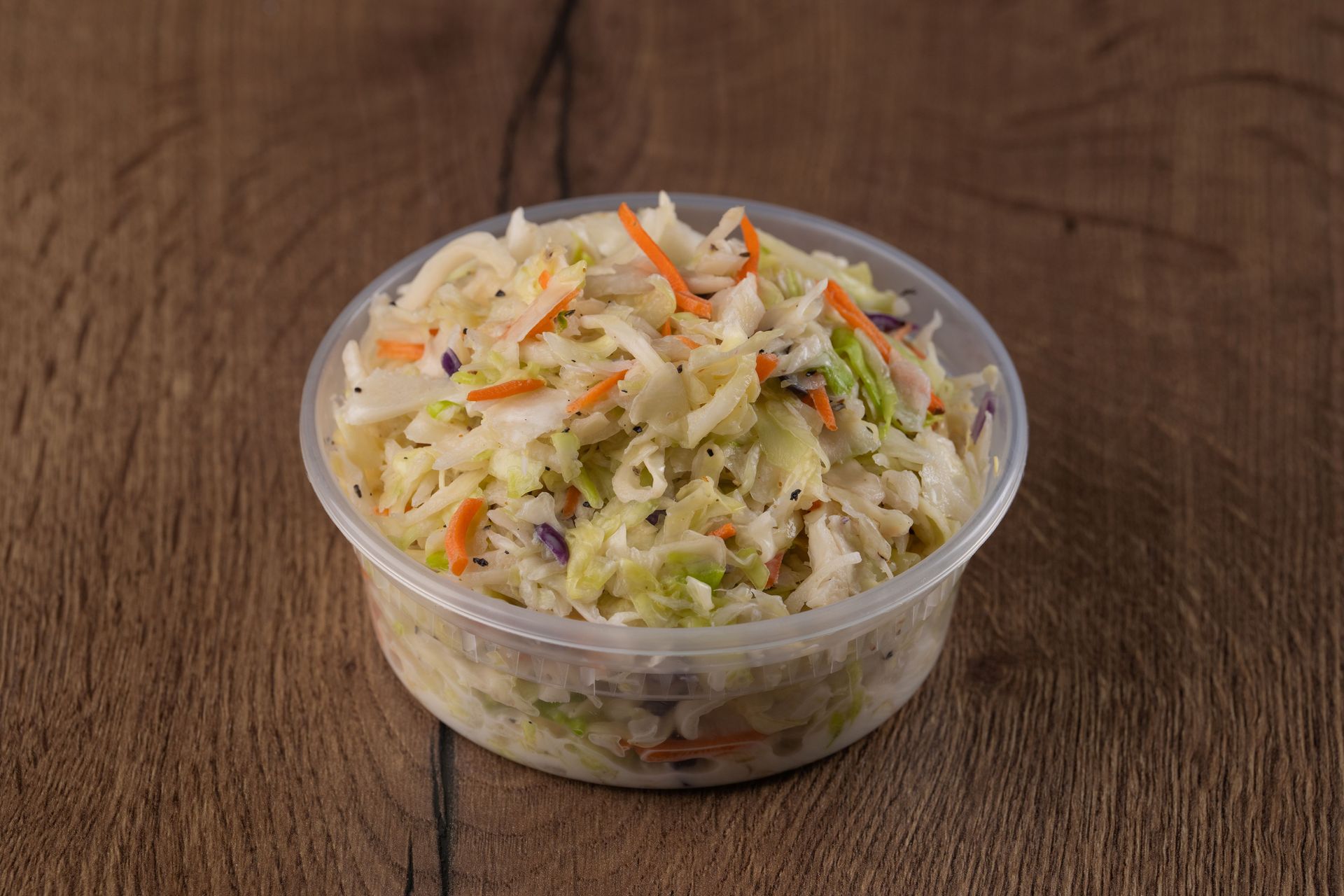 Coleslaw in a clear plastic container on a wooden surface.