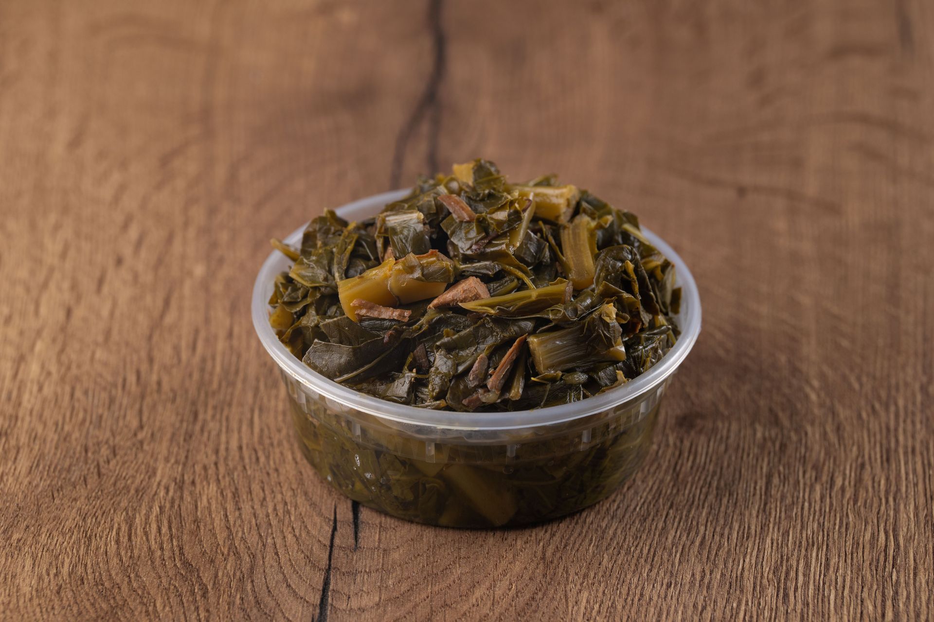 Collard greens in a clear plastic container on a wooden surface.