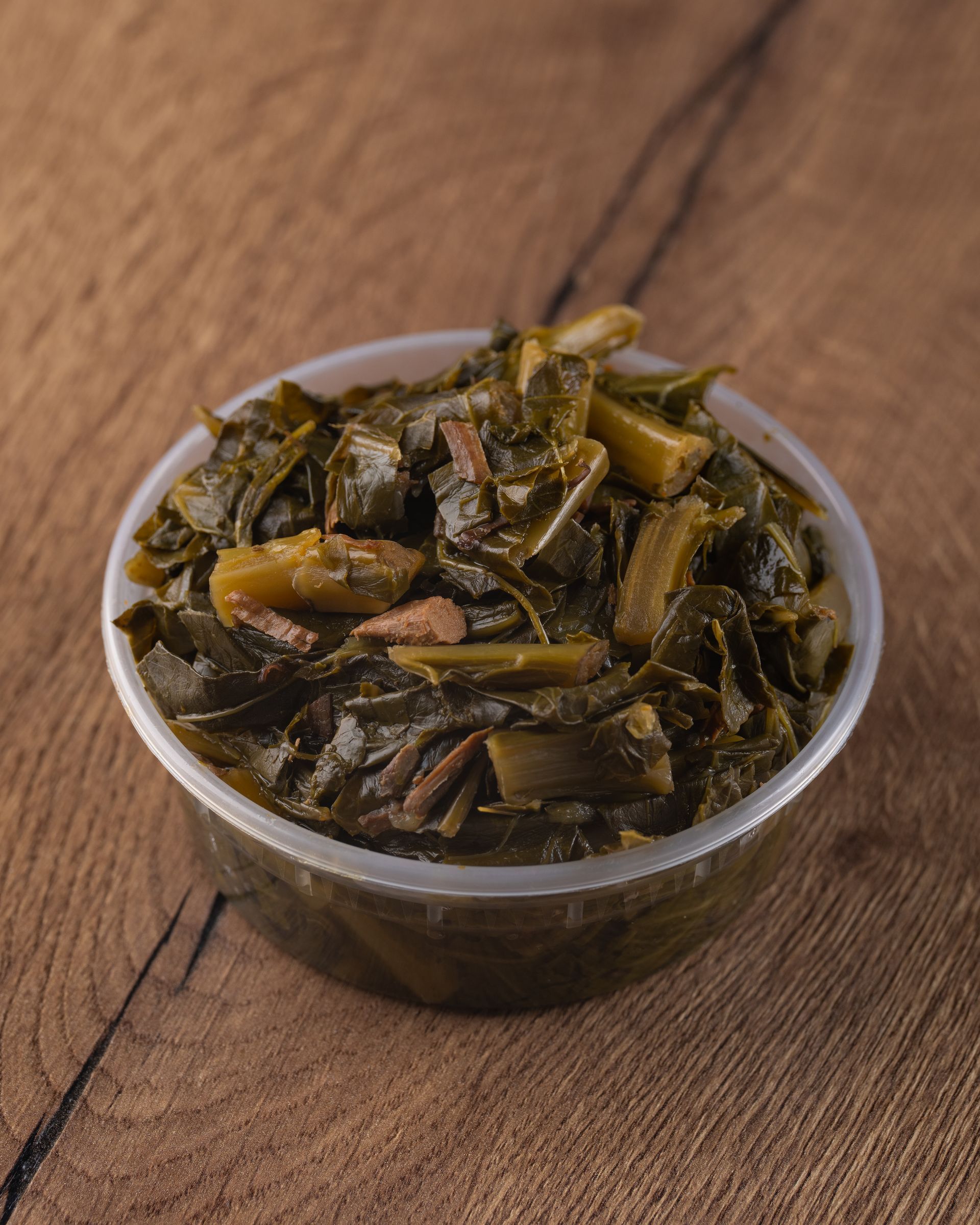Collard greens in a clear plastic container on a wood surface.