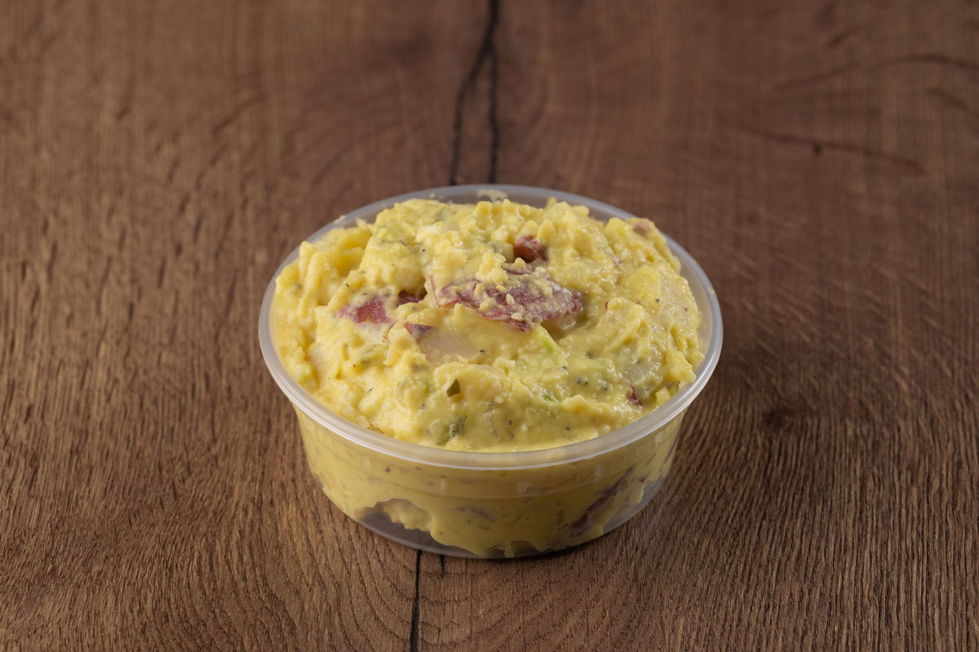 Potato salad in a clear plastic container on a wooden surface.