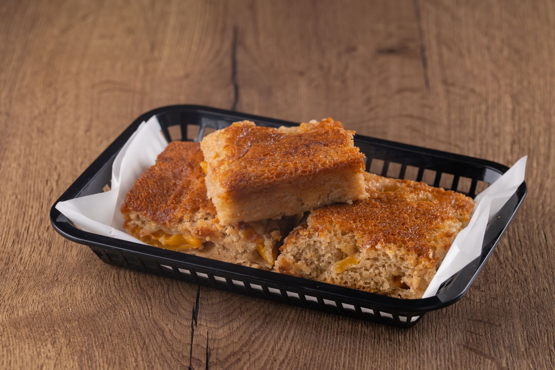 Brown cake slices in a black basket lined with white paper, on a wooden surface.
