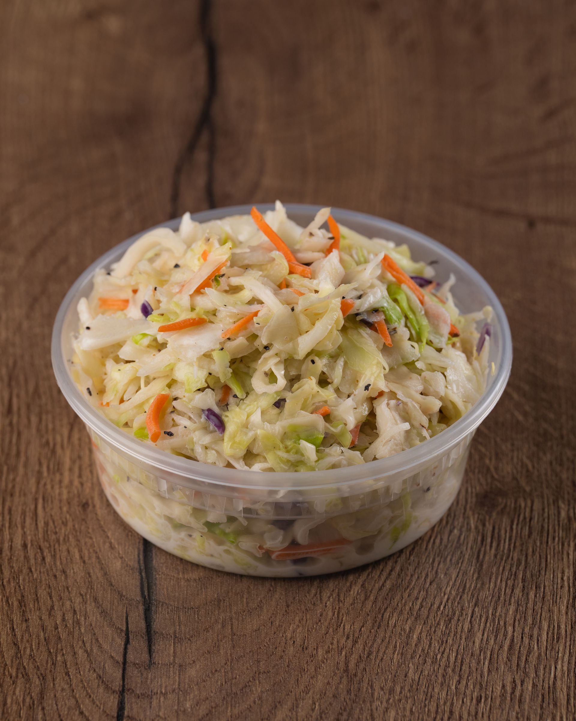 Coleslaw in a clear plastic container on a wooden surface.