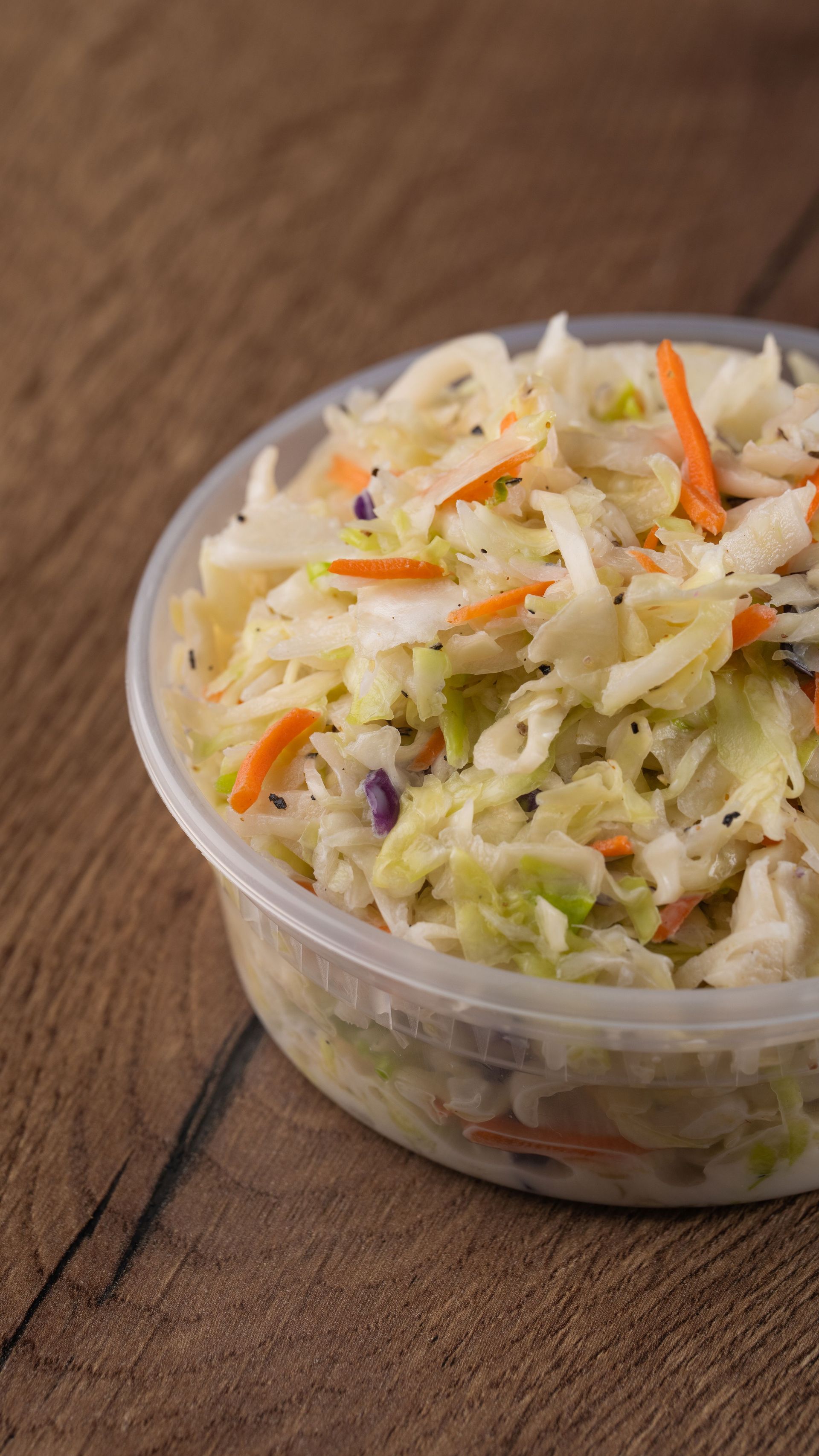 Coleslaw in a clear plastic container on a wooden surface.