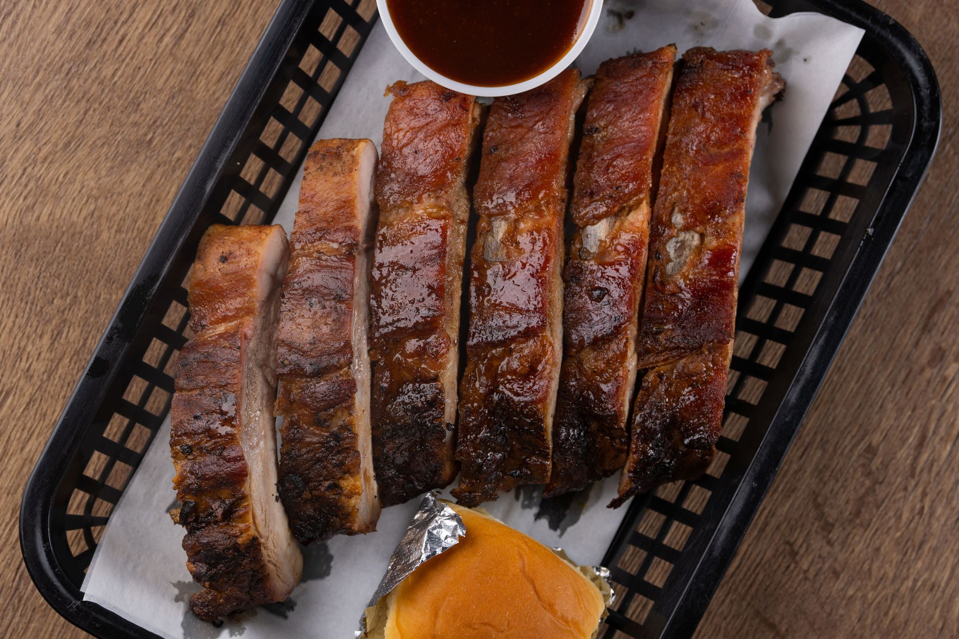 Sliced BBQ ribs with sauce and a roll in a black basket.