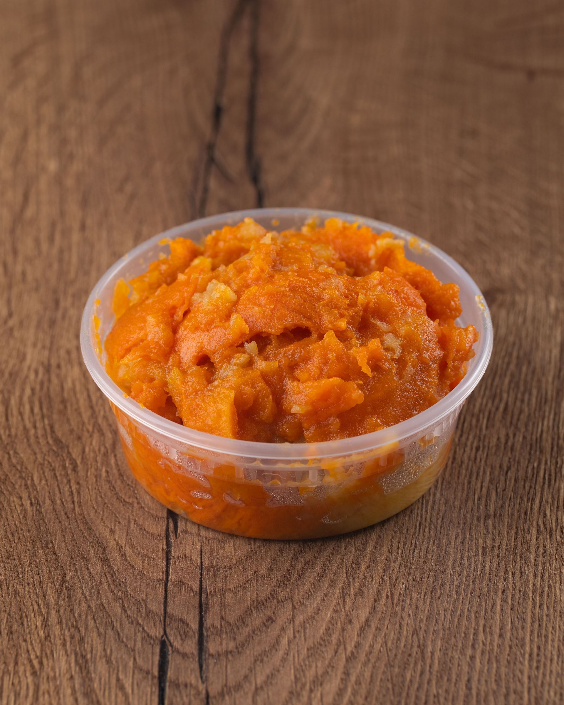 Orange food in a clear plastic container sits on a wooden surface.