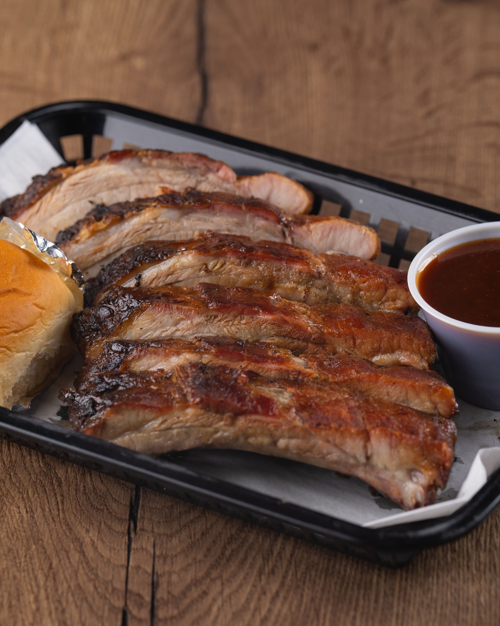 Sliced BBQ ribs with sauce and a roll on a tray.