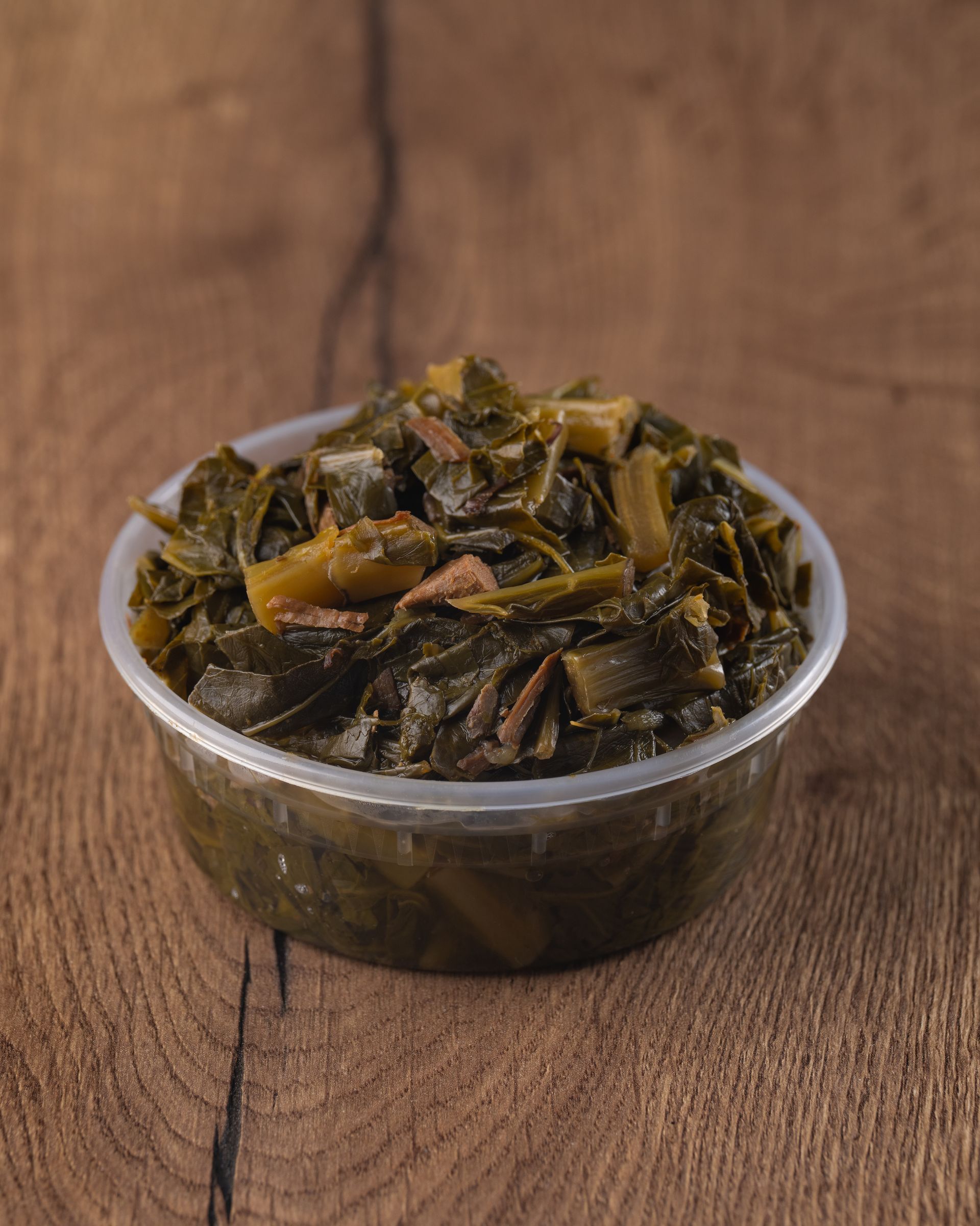 Cooked collard greens in a clear plastic container on a wood background.