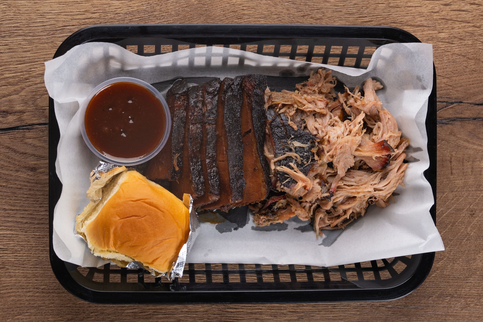 BBQ platter with sliced brisket, pulled pork, sauce, and a bun in a basket.