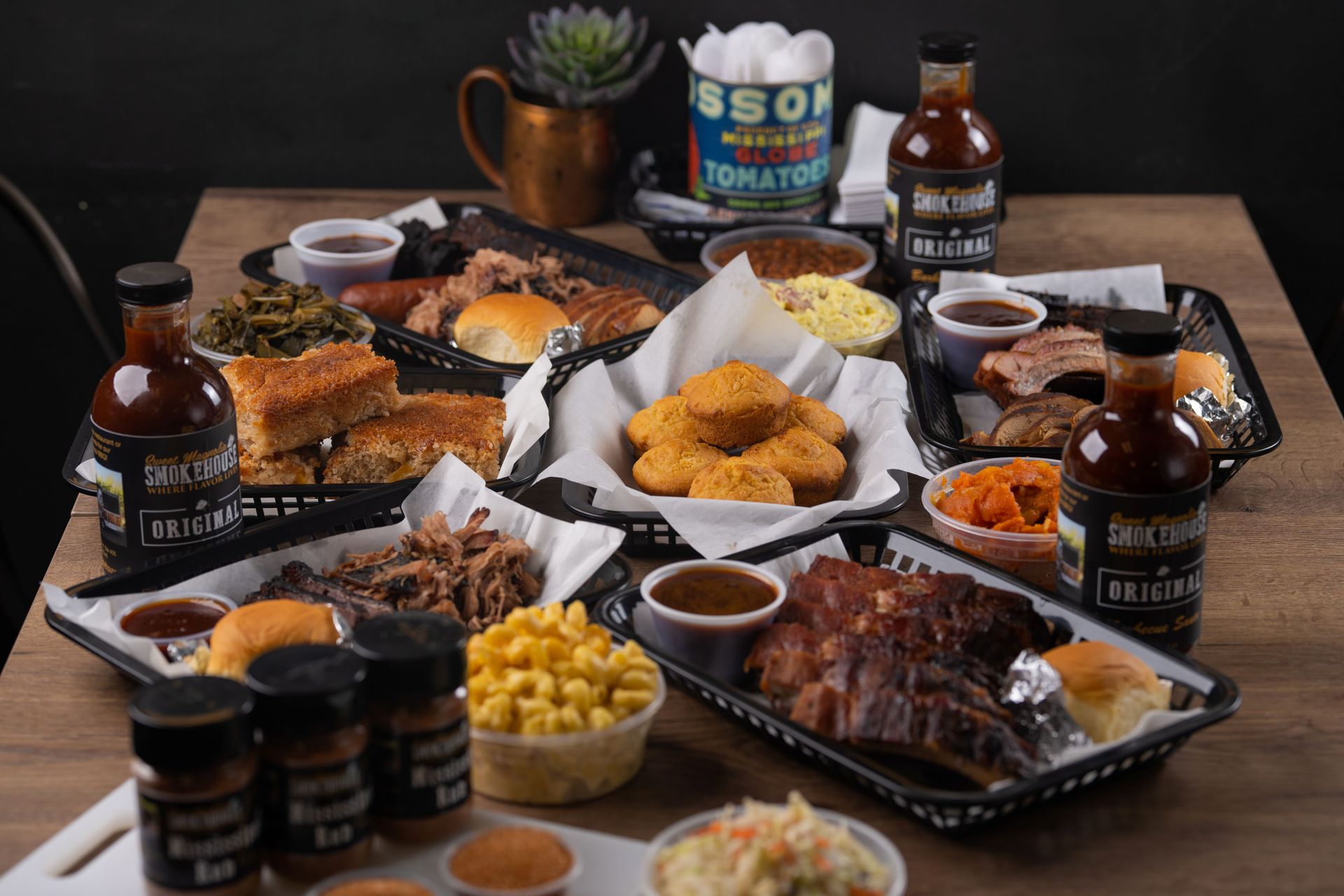 Barbecue spread on a wooden table, featuring ribs, brisket, sides, and sauces.