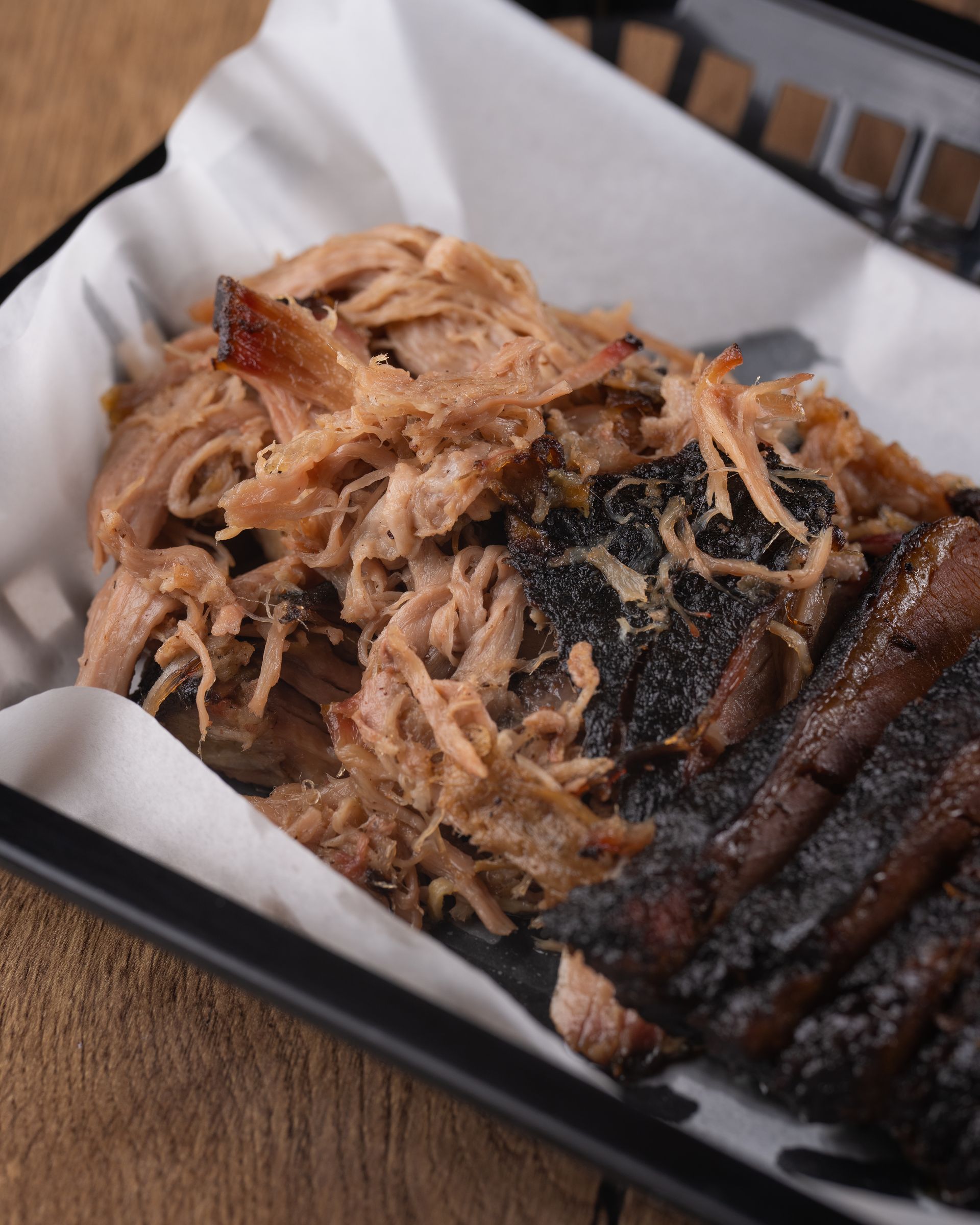 Pulled pork and ribs in a basket lined with white paper, on a wooden surface.
