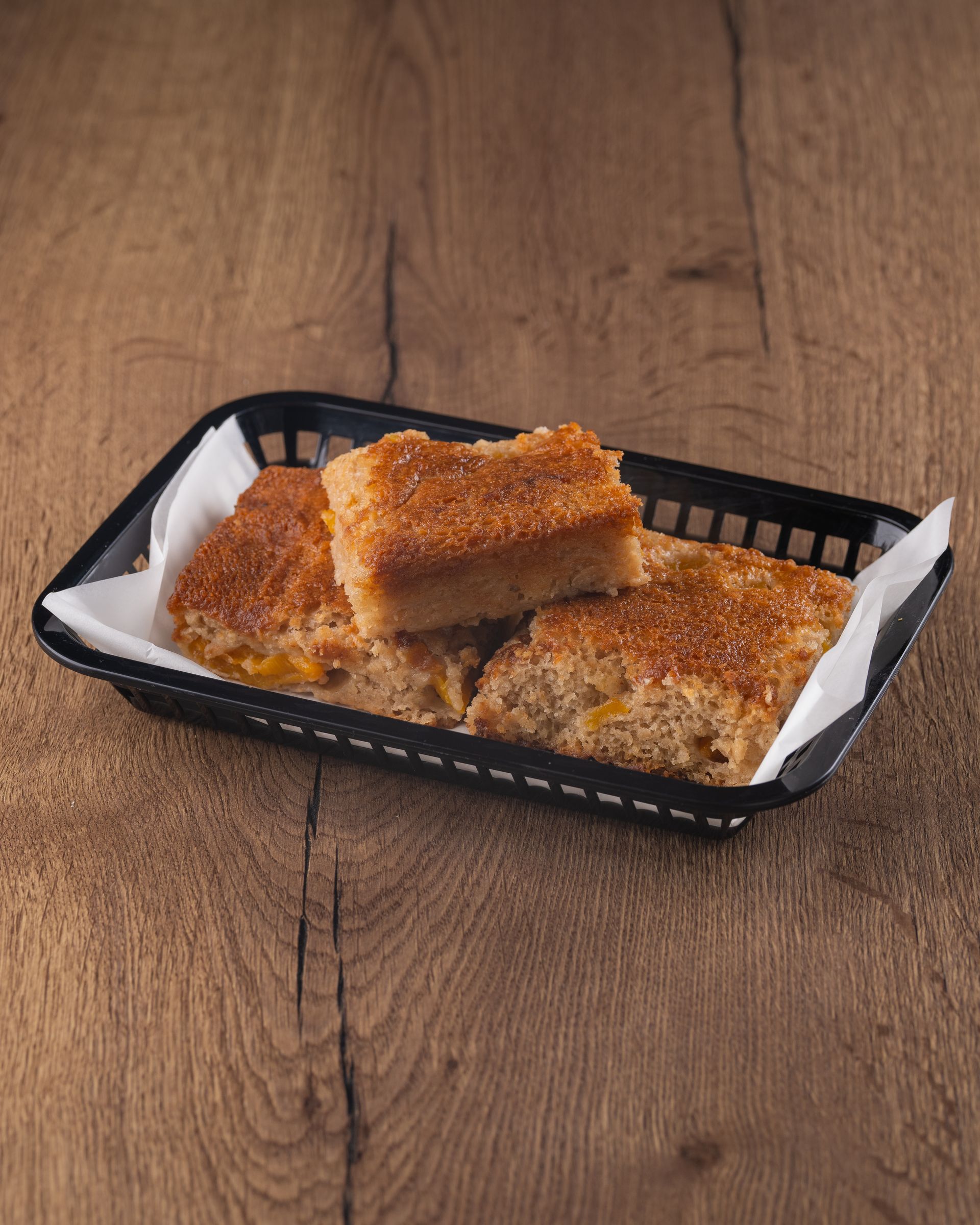 Squares of cornbread in a black basket lined with white paper, set on a wooden table.
