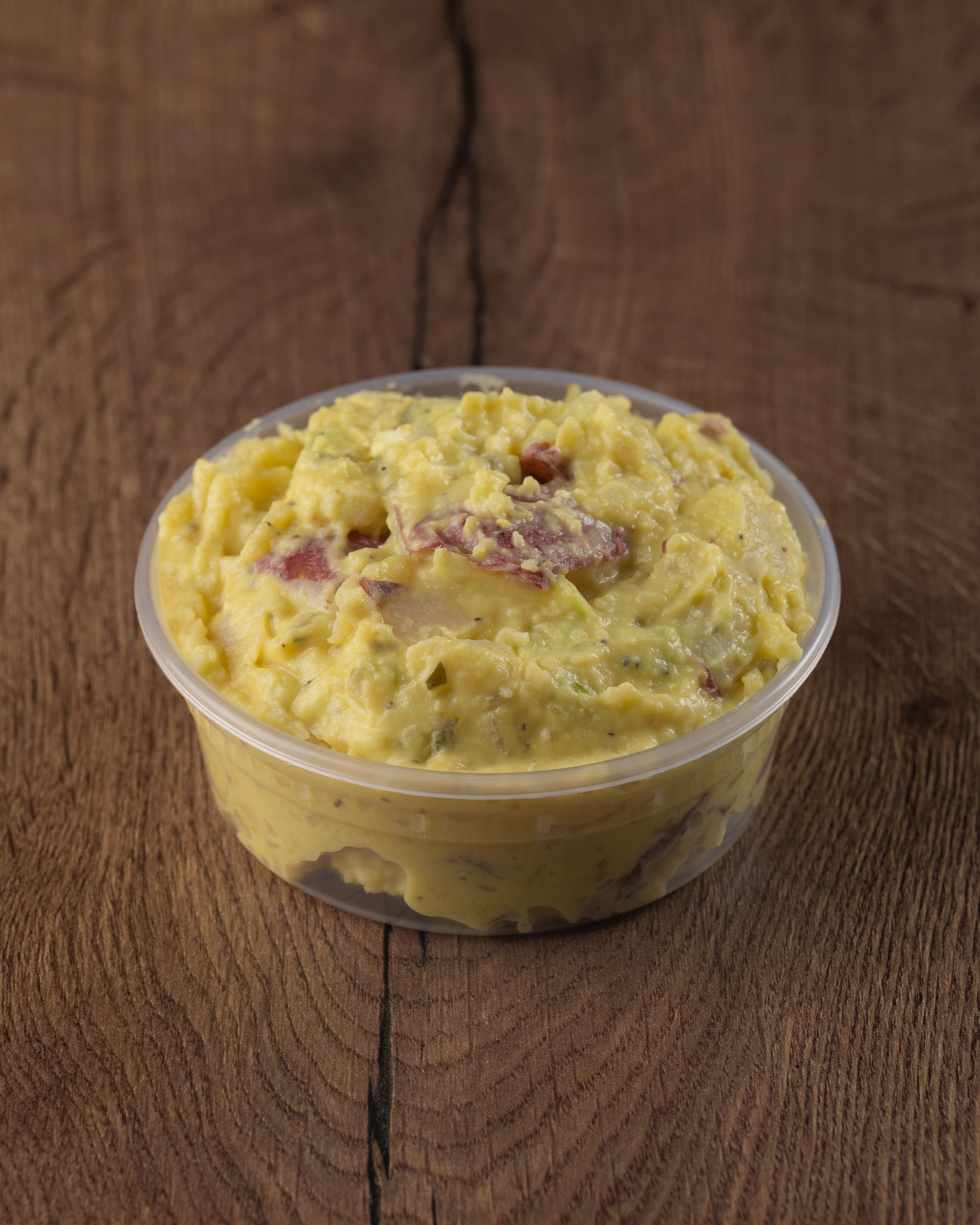 Potato salad in a clear plastic container on a wooden surface.