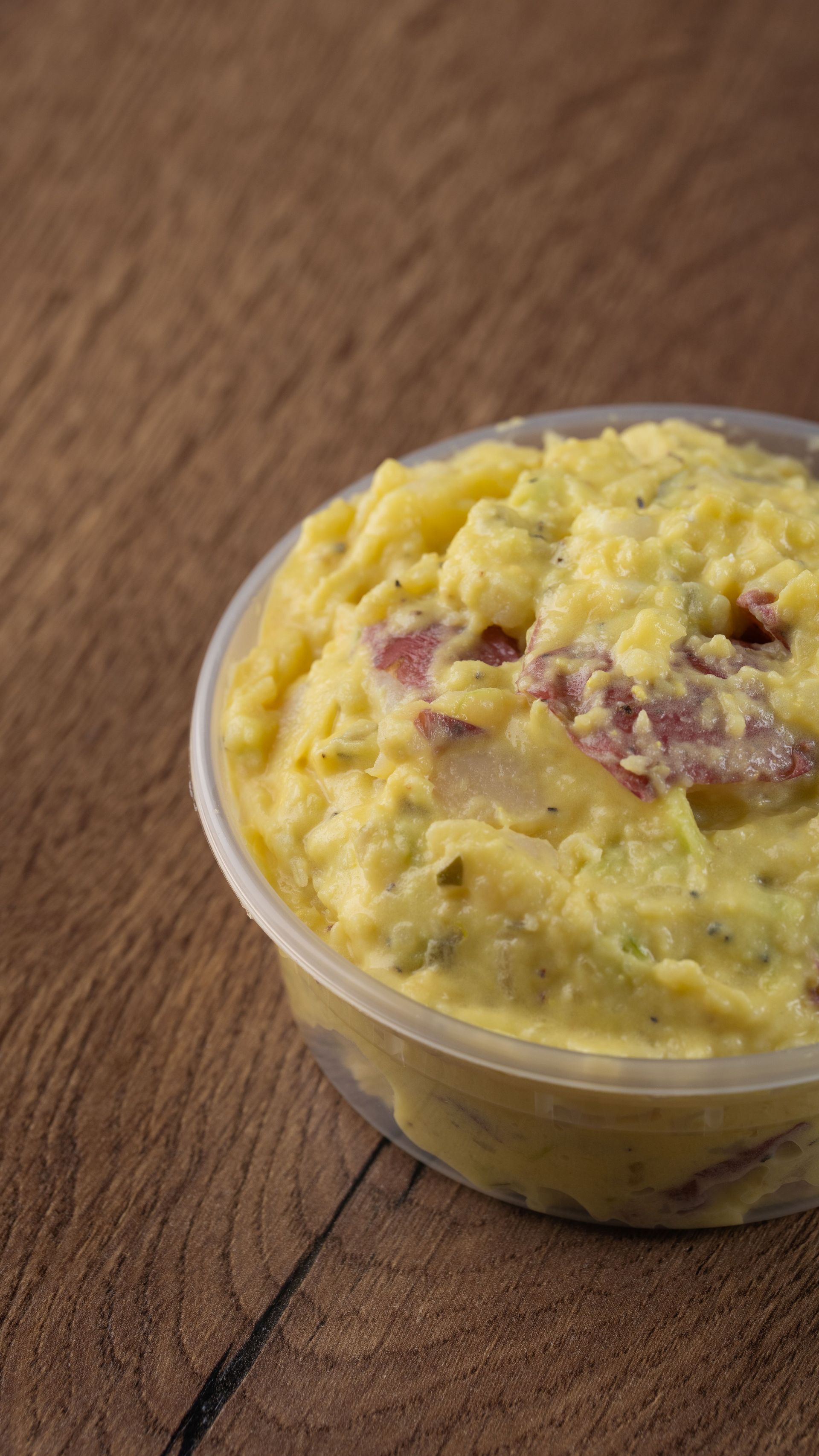 Potato salad in a clear plastic container on a wooden surface.