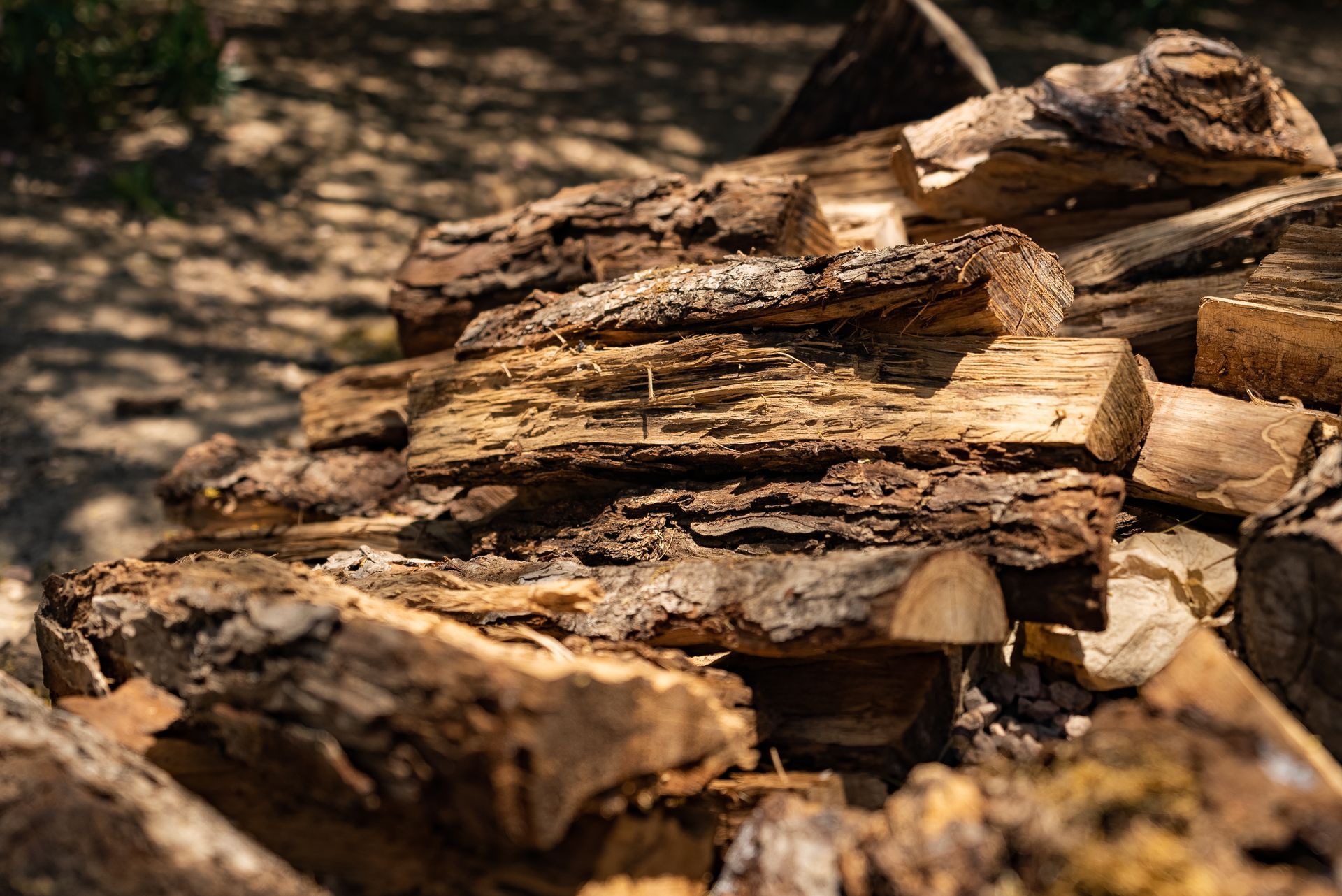 Pile of split firewood in sunlight, with rough bark and varying shades of brown.