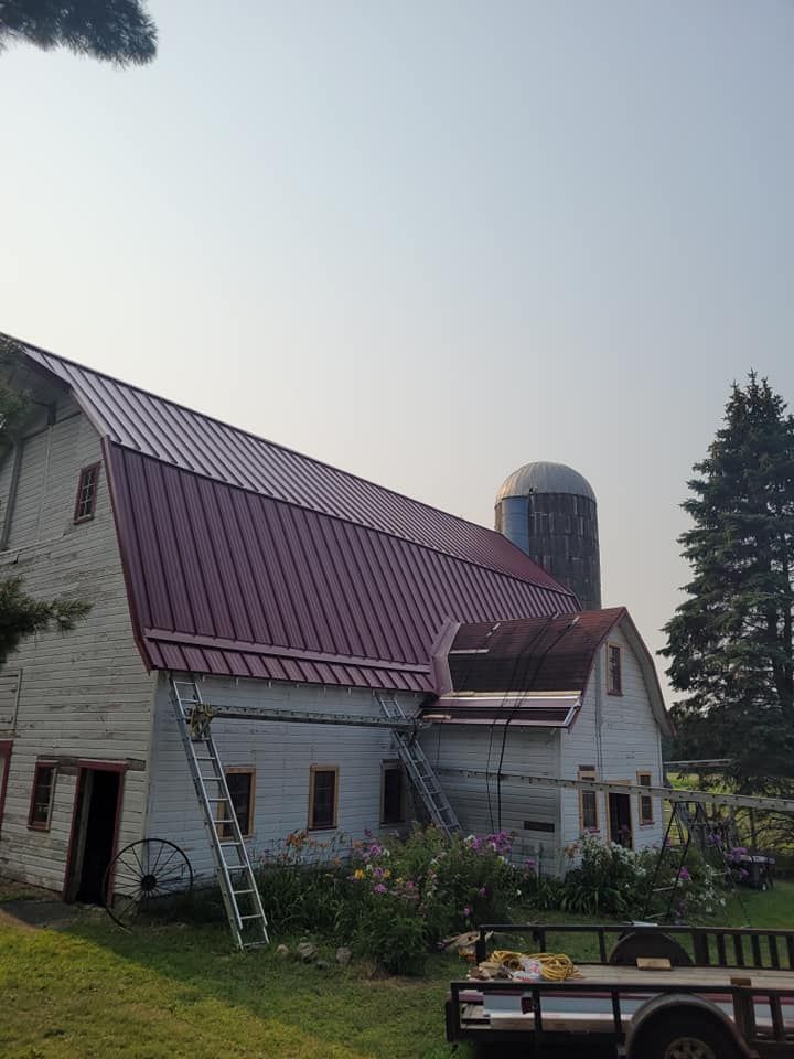 A white barn with a red roof and a trailer parked in front of it.